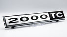 Black and chrome 2000TC badge displayed on a clear stand, studio shot
