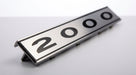 Chrome-edged 2000 badge shown at an angle on a plain grey background