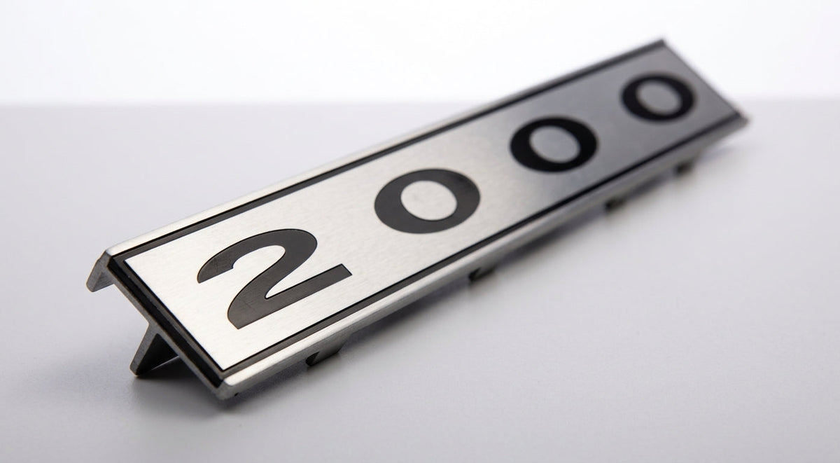 Chrome-edged 2000 badge shown at an angle on a plain grey background