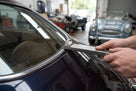 Hands using the metal fitting tool on a classic car's glazing rubber