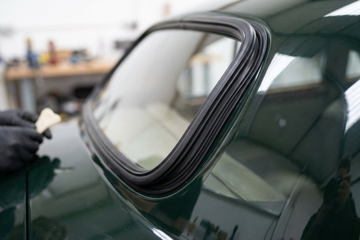 Gloved hand fitting a windscreen seal to the rear quarter window of a green classic Jaguar