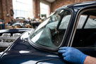Windscreen seal being fitted by a gloved hand to a dark blue classic Jaguar E-Type