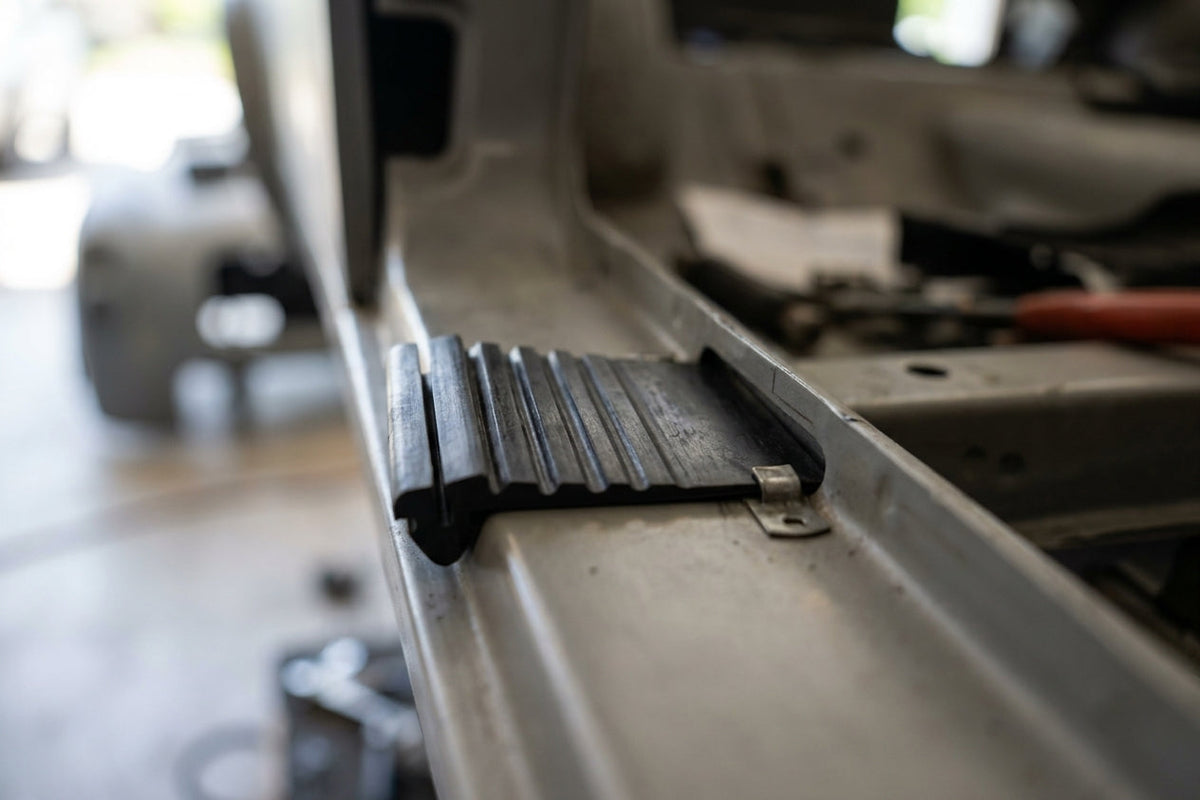 Black ribbed rubber flap fitted to the sill of a Triumph Stag, workshop background