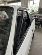 Black window seal fitted around a white Escort's front door glass, workshop