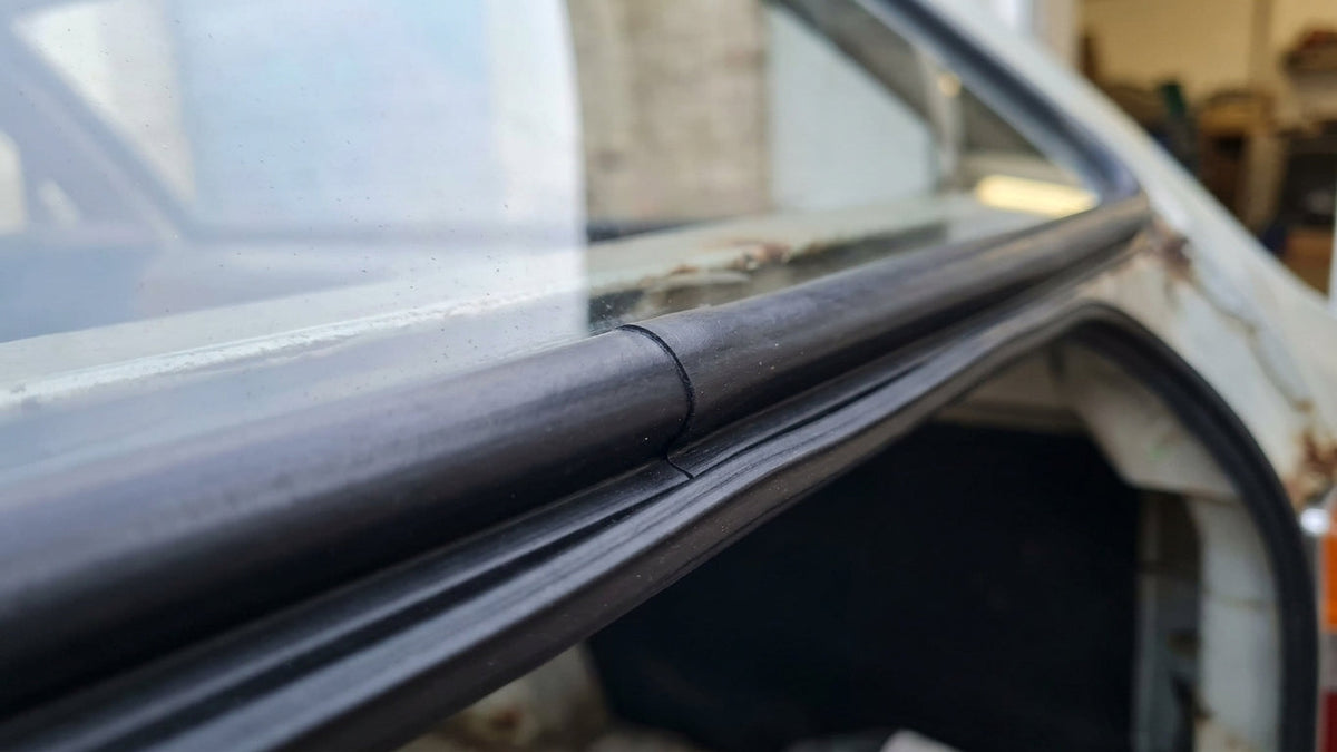 Black tailgate seal fitted along a white estate car's rear door edge, close-up joint