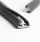 Dark grey edge trim shown end-on with a white plastic fixing clip inside the channel