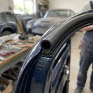 Side seal fitted to a dark blue classic car roof edge in a workshop with a classic car behind