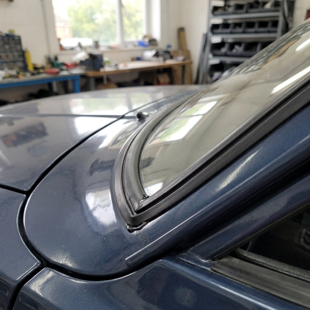 Black windscreen seal fitted around a dark blue Cortina's screen corner, workshop