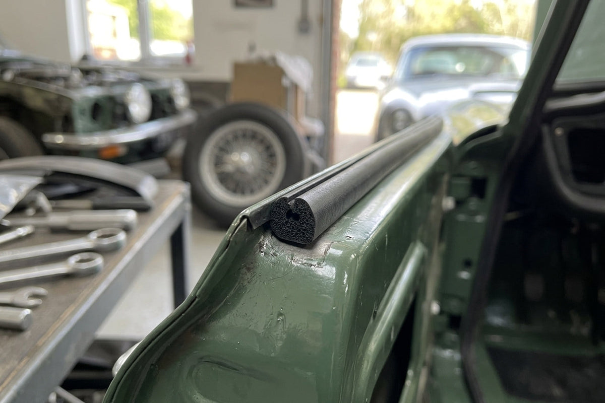 Sponge strip fitted along a green car's door edge, tools on bench behind