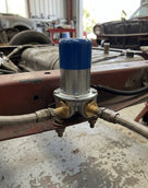 Fuel pump with blue cap fitted to a chassis rail with braided fuel lines, classic cars behind