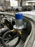 Fuel pump with blue cap fitted to the inner wheel arch, classic car workshop in the background