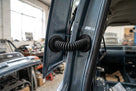 Black tailgate grommet bridging a blue car's open tailgate hinge, close-up
