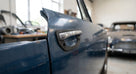 Chrome door handle on a blue Triumph Stag door with black gasket seated behind it