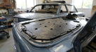 Black perforated seat diaphragm panel laid on a Triumph Stag bonnet, wire clips visible