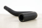 Black ribbed rubber heater hose with a bend, studio shot on a light surface