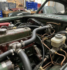 Black hose connected between engine components under the bonnet of a green classic car