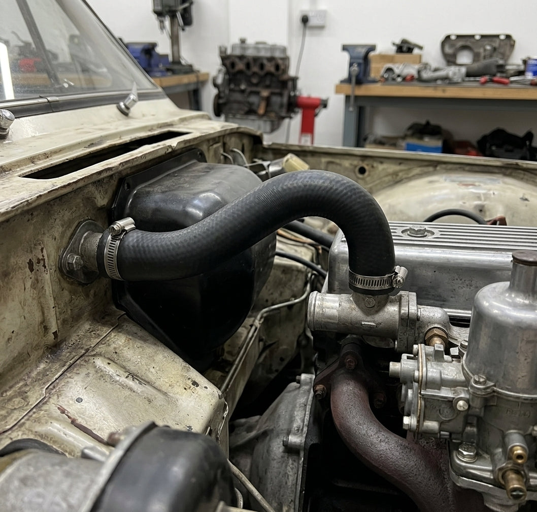 Black heater inlet hose looping over the heater box to the bulkhead in a part-stripped Herald engine bay