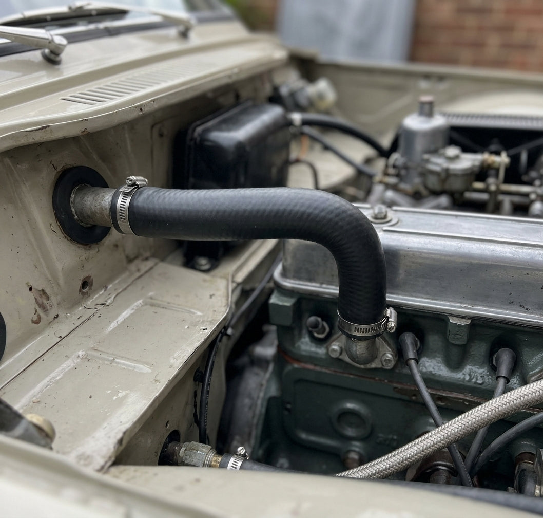 Black heater hose fitted through the bulkhead of a cream classic car engine bay