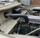 Black heater hose fitted through the bulkhead of a cream classic car engine bay