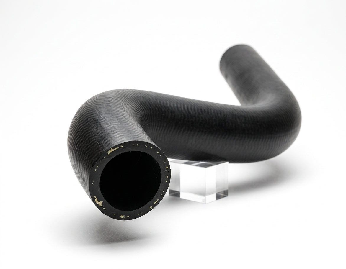 Black textured rubber radiator hose with bent profile, cut end facing camera on studio plinth