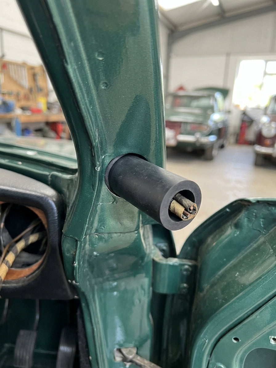 Black rubber sleeve pushed over a wiring loom stub on the green door pillar of a classic car in a workshop