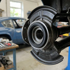 Black seal fitted around a rear hub assembly, blue classic car in background