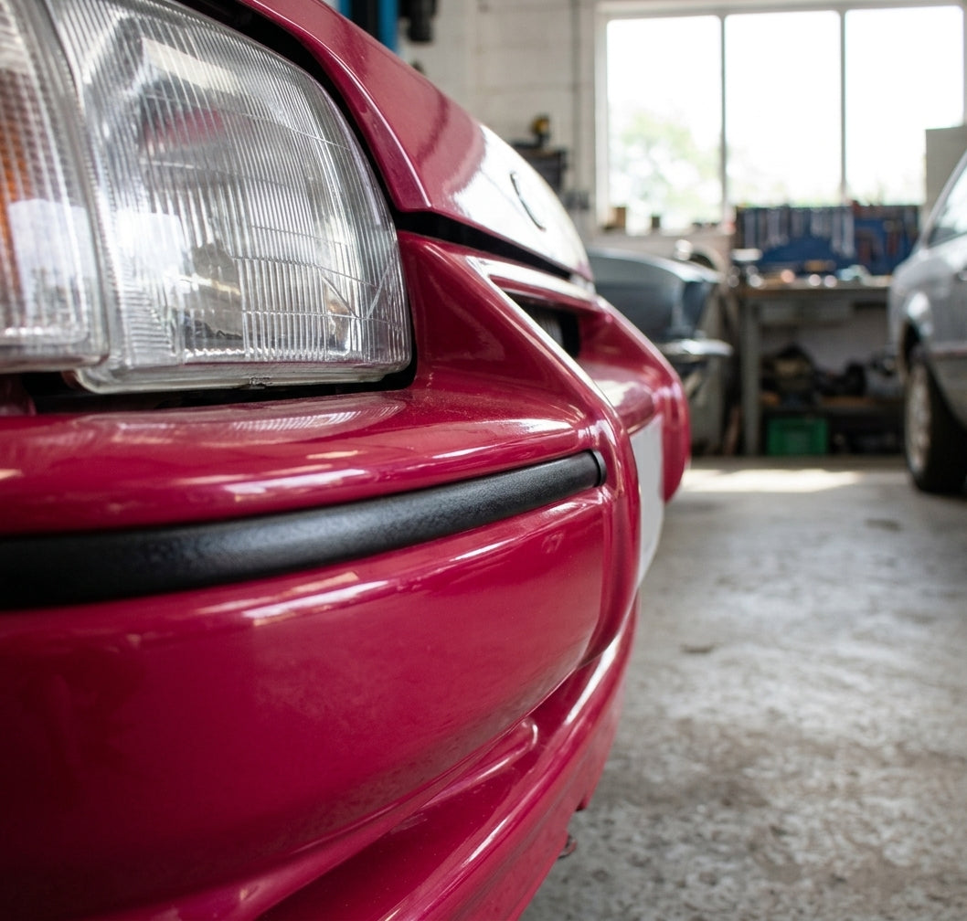 Satin black trim fitted along a red car's bumper edge, close-up workshop shot
