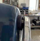 Black rubber mounting bush fitted between a blue wing and chrome bumper bracket