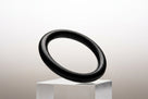 Black nitrile O-ring balanced on a clear plinth, studio shot