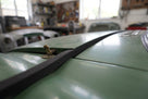 Thin black foam strip fitted along a green classic car's bonnet centre seam