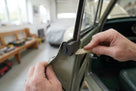 Hands fitting a black foam strip into a green classic car's door channel