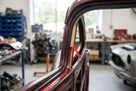 Self-adhesive foam strip with red peel tab fitted along a maroon classic car's door frame