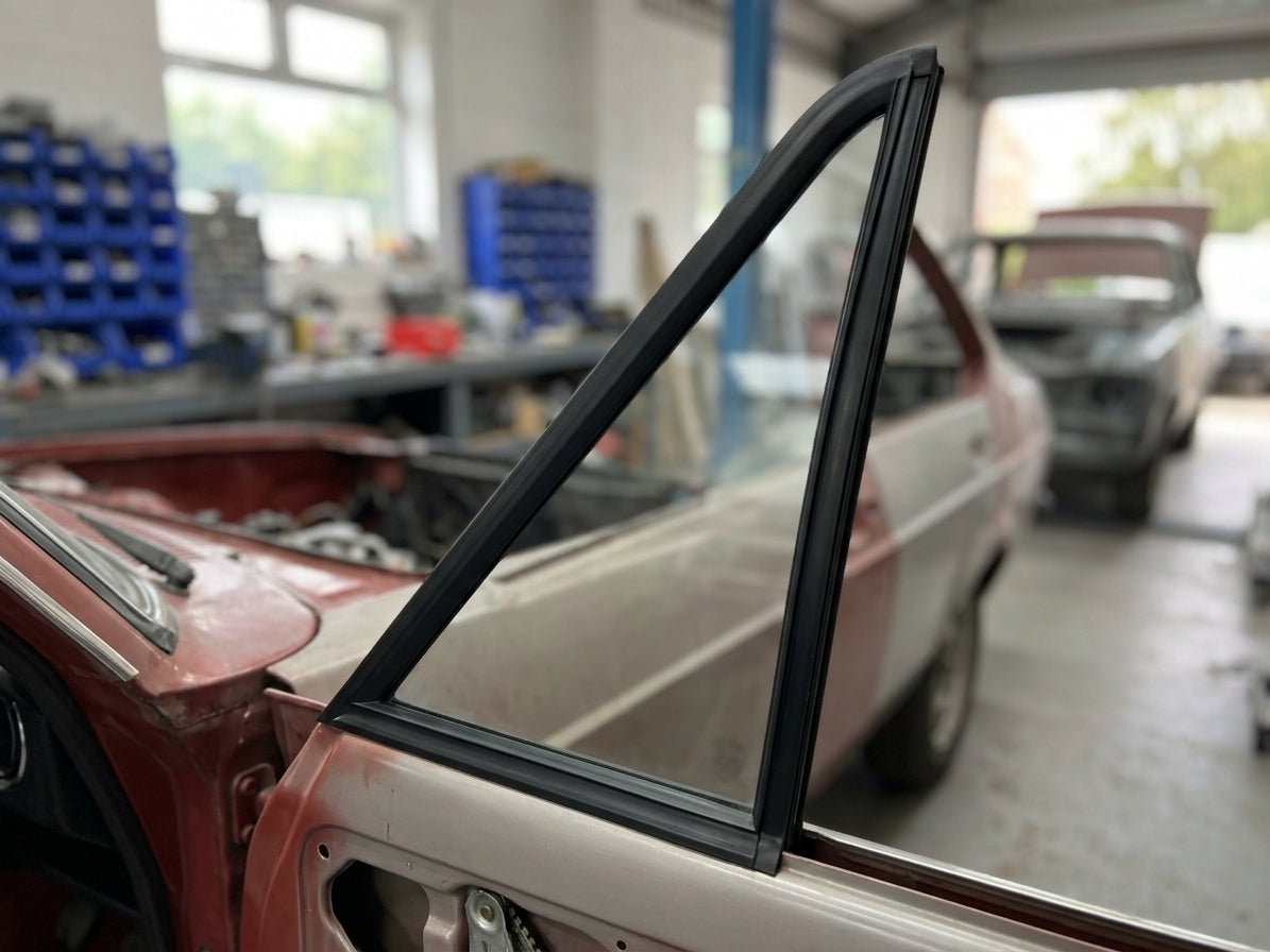 Black quarterlight seal on a part-painted red and cream Escort Mk2 front window, workshop behind