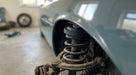 Front coil spring and suspension arm of a light blue classic car on a ramp