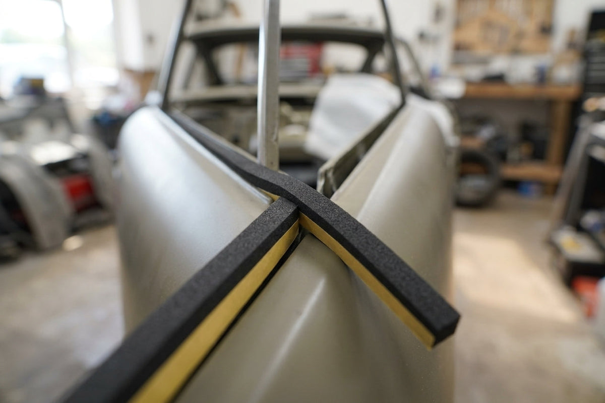 Black sponge strip applied along the roof edge of an unpainted classic car shell in a workshop
