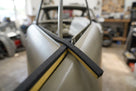 Black sponge strip applied along the roof edge of an unpainted classic car shell in a workshop