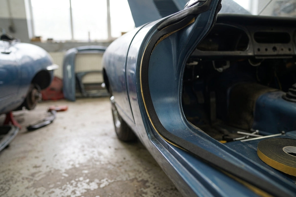 Black sponge seal fitted to a door shut face of a blue classic car, roll of tape in the foreground