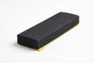 Black sponge strip block with yellow adhesive backing peeled out from underneath, studio shot