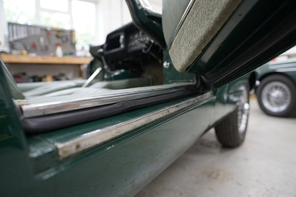 Black sponge strip fitted along a sill edge beneath an open door of a green classic car