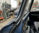 Black sponge seal fitted along the door frame of a dark blue classic car