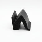 Black sponge rubber section with zigzag M-shaped profile, cut end showing porous cell structure