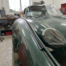 Black trim fitted to a wing edge on a green classic car, bonnet open behind