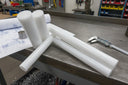Several white PTFE rods of differing diameters stacked on a bench with callipers and drawings