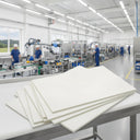Stack of white HDPE sheets fanned on a bench in a bright factory, assembly line and staff behind