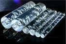 Six clear bubble acrylic rods on a black reflective surface, trapped bubbles catching the light
