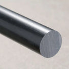 Charcoal-black HDPE rod angled towards the camera, sawn end face lit against a mottled stone-beige backdrop