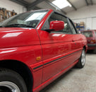 Black door moulding fitted along a red convertible Escort's waistline, workshop shot