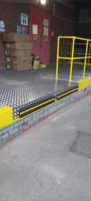 Loading dock edge in a warehouse, chequer-plate deck with a yellow and black striped lip and yellow safety rail