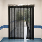 Black mesh fly screen strip curtain on a stainless hook-on rail in a tiled kitchen doorway, one strip pushed aside
