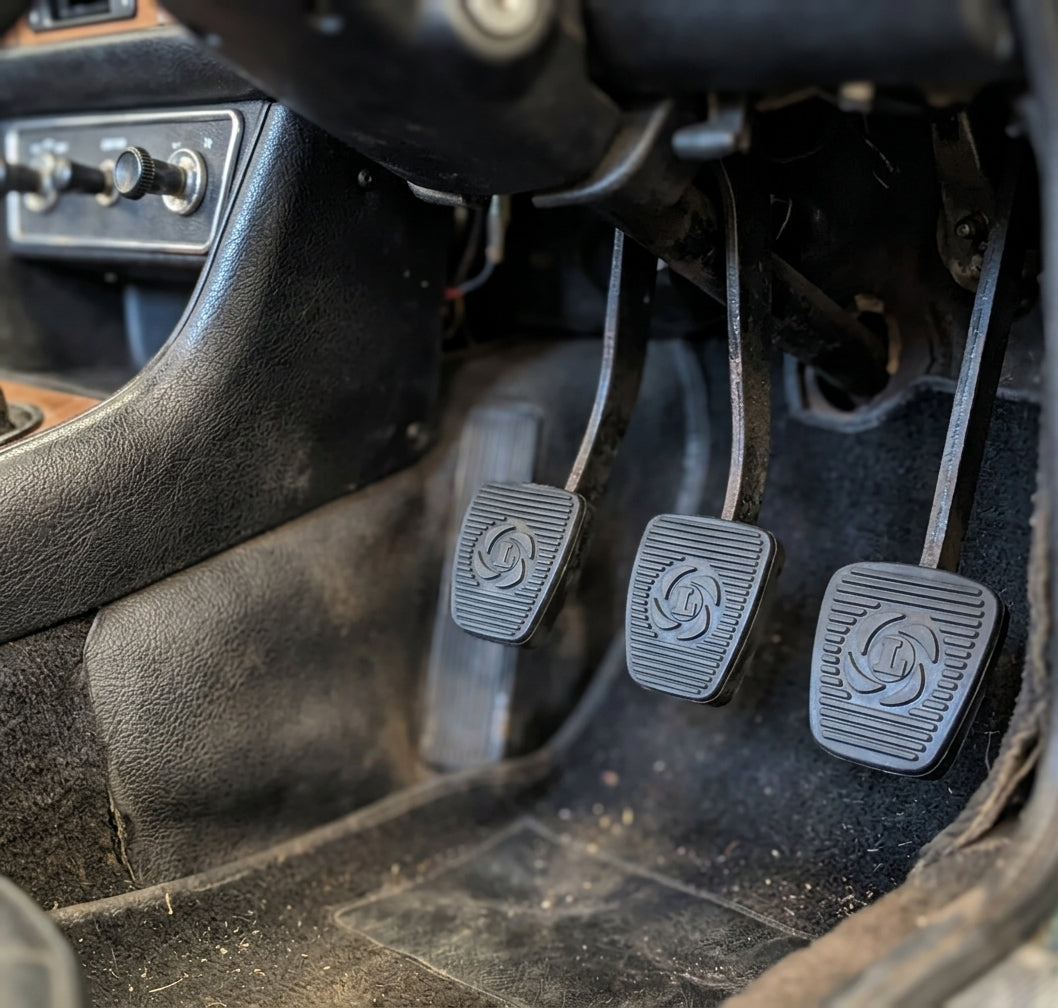 Three black ribbed pedal pads fitted in a Triumph Stag manual footwell